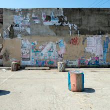 A wall covered in graffiti and old signs in a parking lot with decoratively painted stumps as stools